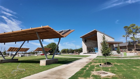 Modern outdoor pavilion with angled wooden roofs and a stone building under a clear blue sky.