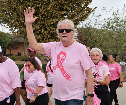 Mayor Ron Jensen wearing a Pink Out shirt and waving at the camera surrounded by other walkers.