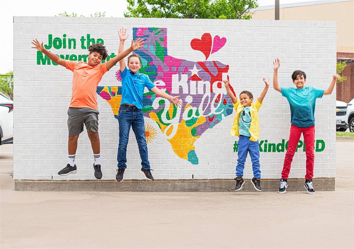 Four kids jumping in front of a mural that says 