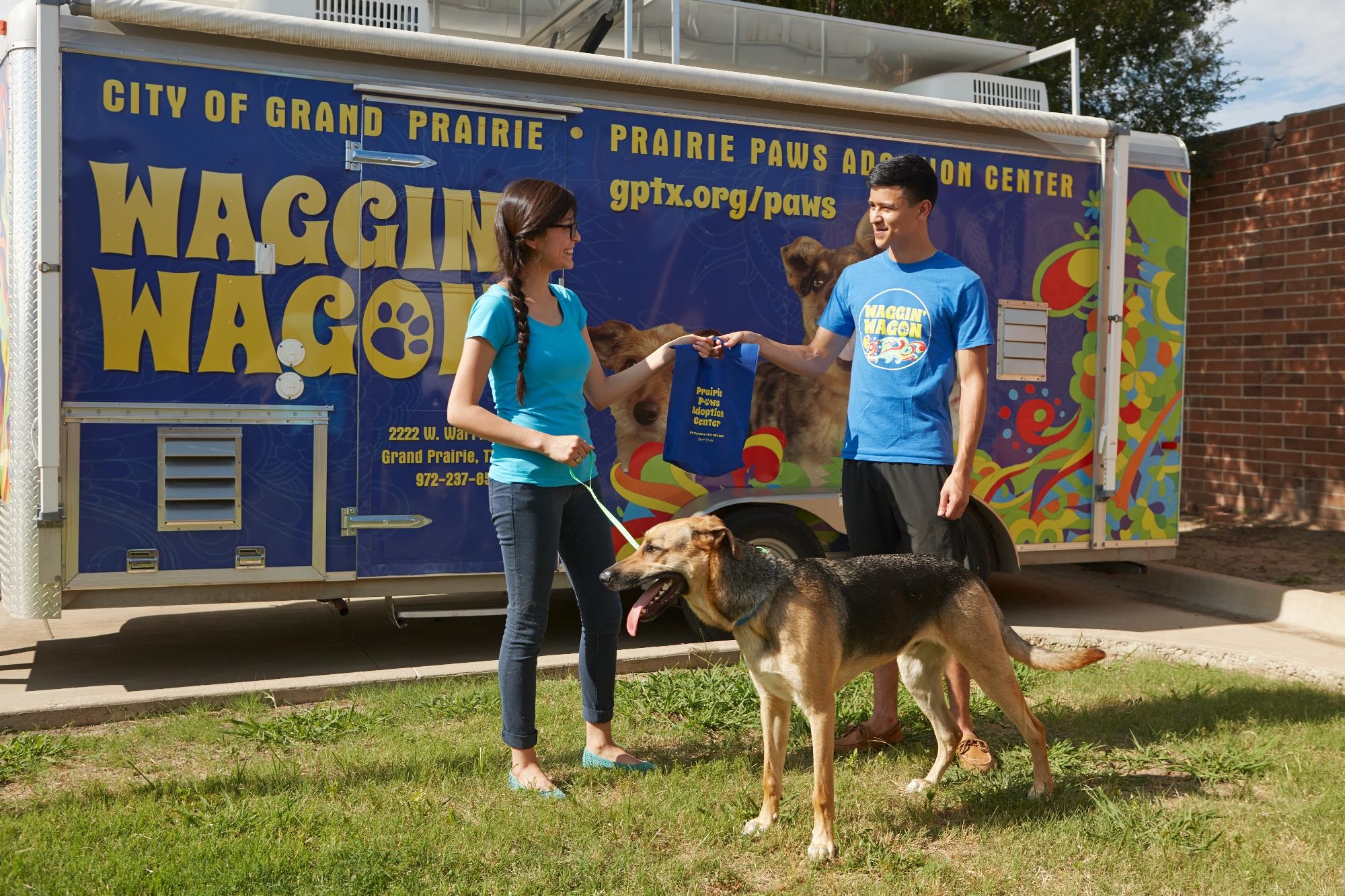 Two people and a dog are standing in front of the Waggin Wagon