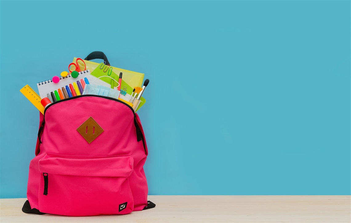 Pink backpack with school supplies in it, in front of a blue background