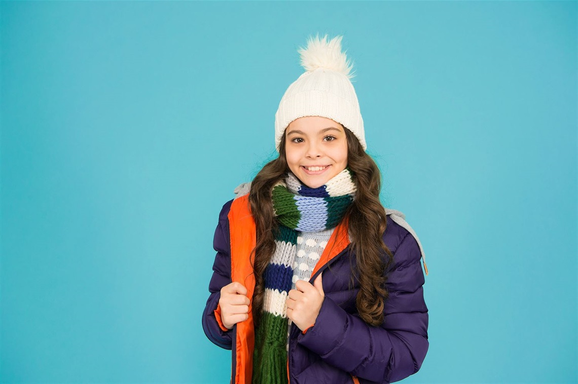 Girl wearing a winter coat, scarf, and hat smiling at the camera