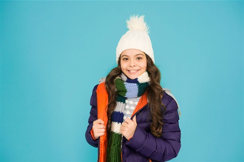 Girl wearing a winter coat, scarf, and hat smiling at the camera
