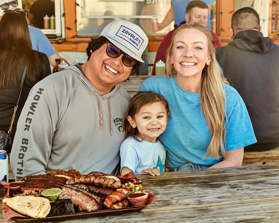Picture of Joe Zavala and his family sitting at a table at Zavala's Barbecue and smiling at the camera