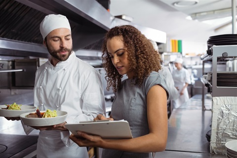 Person holding a clipboard is talking to a chef in a commercial kitchen
