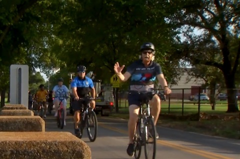 Mayor Ron Jensen and some other people are riding their bikes. Jensen is waving at the camera.