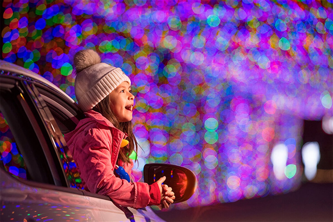 Girl leans out of a car window and gazes at a display of holiday lights